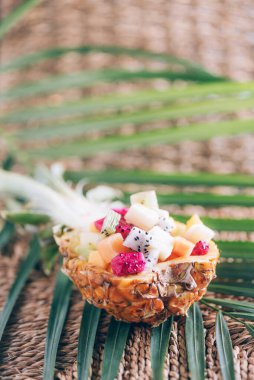 Tropikal meyve salatası ananas arkaplanındaki palmiye yapraklarının üzerinde servis edilir. Uzayı kopyala Tropik seyahat, egzotik meyve. Vejetaryen ve vejetaryen kavramı.