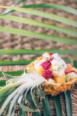 Tropikal meyve salatası ananas arkaplanındaki palmiye yapraklarının üzerinde servis edilir. Uzayı kopyala Tropik seyahat, egzotik meyve. Vejetaryen ve vejetaryen kavramı.