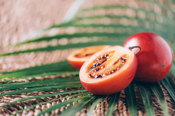 Buah Tamarillo atau terong belanda dengan daun palem pada latar belakang rotan. Salin ruang. Perjalanan tropis, buah eksotis. Konsep vegetarian dan vegan — Stok Foto