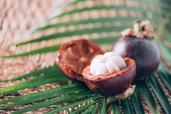 Mangosteen pálmalevéllel, rattan háttérrel. Másold a helyet. Trópusi utazás, egzotikus gyümölcs. Vegán és vegetáriánus fogalom — Stock Fotó