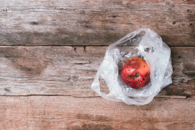 Ahşap arka planda plastik poşette bozulmuş kırmızı elma. Çöp yığını çürük yiyecekler. Üst Manzara. Uzayı kopyala Çürük sebze ve meyve konsepti. Sıfır atık, gübre