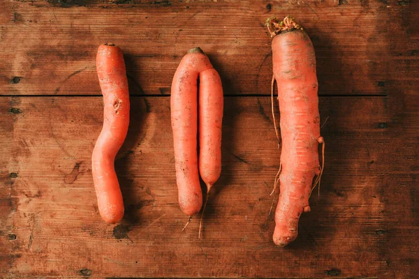 Zanahorias feas deformadas sobre fondo de madera. Concepto de producción de cero residuos. Vista superior. Copiar espacio. Hortalizas no gmo — Foto de Stock