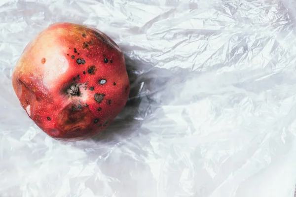 Spoiled bad red apple on plastic bag background. Garbage dump rotten food. Top view. Copy space. Rotten vegetables and fruits concept. Zero waste, compost