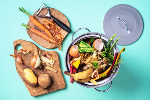 Recycler les déchets de cuisine. Vie durable et zéro déchet. Déchets végétaux en pot de compostage de recyclage. vue de dessus. Espace de copie. Légumes pelés sur planche à découper, bac à compost blanc sur fond bleu . — Photo