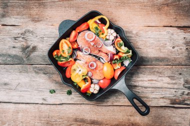 Sağlıklı yiyecekler. Yemek malzemesi. Çiğ somon balığı, sebzeler, otlar, baharatlar ahşap zemin üzerinde demir ızgara tavasında. Üst görünüm, alanı kopyala