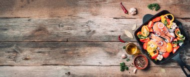 Ahşap arka planda sebzeli somon bifteği. Üst Manzara. Pişirme malzemeli çiğ somon filetosu: yağ, şifalı otlar, kaşık ve çatal. Banner, boşluğu kopyala