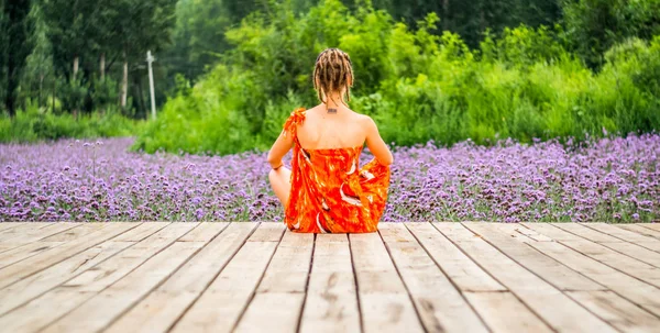 Une femme avec des dreadlocks est assise sur une jetée en bois avec des fleurs — Photo