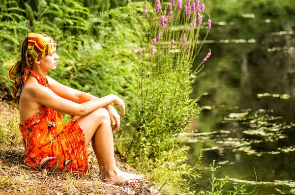 Una mujer está sentada en la orilla del río mirando lejos —  Fotos de Stock
