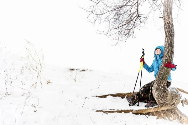 Menina caminhante tendo descanso na encosta nevada sentado em uma árvore no inverno — Fotografia de Stock