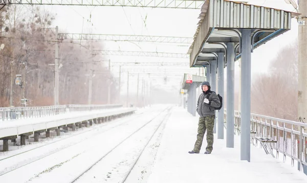 Joven serio con barba de pie en la estación de tren vistiendo abrigo caliente en invierno en clima nevado — Foto de Stock