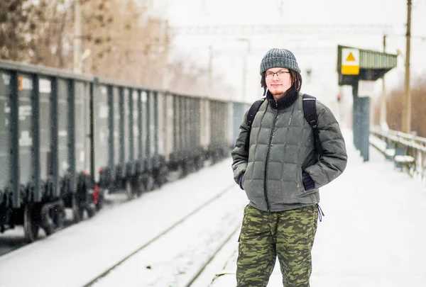 man is waiting for a train at the railway station outdoors in snow in winter