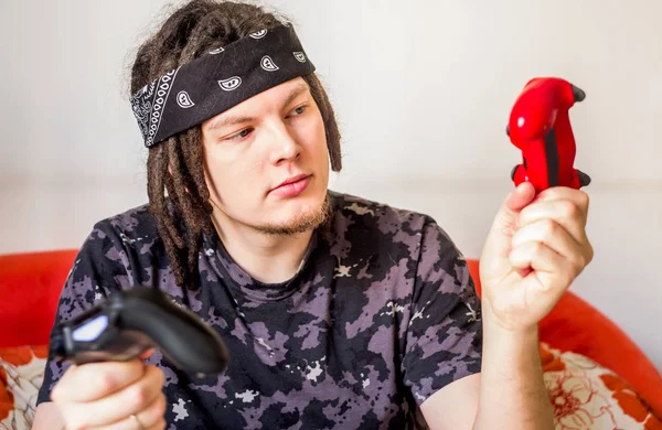 Joven con rastas jugando videojuegos mirando el controlador de juego th sentado en un sofá naranja — Foto de Stock