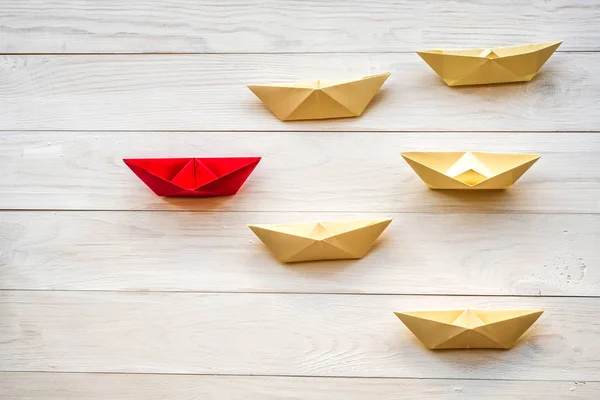 origami paper boats follow a leader on white rustic background