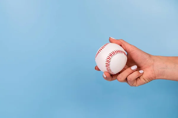 Beyaz tırnaklı bir kadın, mavi arka planda beyaz beyzbol topu tutuyor. — Stok fotoğraf