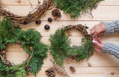 Kadın elleri ahşap arka planda Noel çelengi yapıyor.