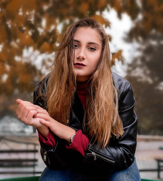 Mujer joven con el pelo largo sentado en un banco en un día de otoño —  Fotos de Stock
