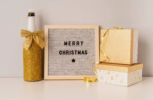 Tablica filcowa Merry Christmas ozdobiona złotą butelką szampana i pudełkami prezentów — Zdjęcie stockowe