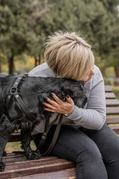 Mujer joven abrazando a su perro cocker spaniel en el banco en el parque — Foto de Stock