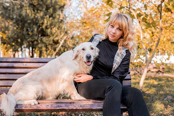 Blonde Kaukasierin sitzt mit ihrem goldenen Labrador-Retriever-Hund auf der Parkbank — Stockfoto