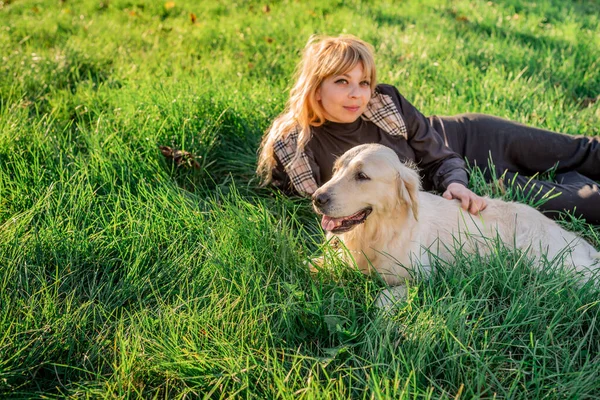 Schöne kaukasische Frau im Gras liegend mit ihrem goldenen Labrador Retriever Hund in einem Park bei Sonnenuntergang — Stockfoto