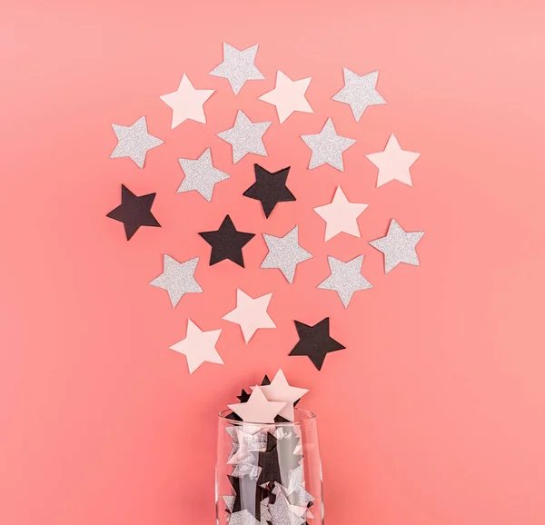 Estrella en forma de confeti que vierte fuera del vidrio sobre fondo rosa plana vista superior —  Fotos de Stock