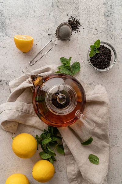 Чайник з чорним чаєм, прикрашений листям м'яти, лимонами і сухим чайним листям зверху квартира лежала — стокове фото