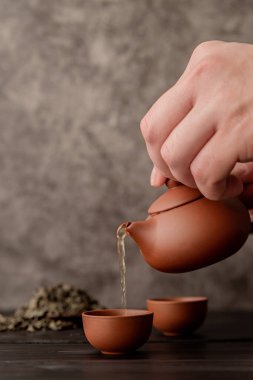 Erkek eli çay fincanının içine koyu arkaplanda çay koyuyor.