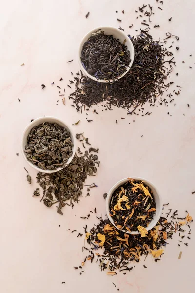 Различные сухие листья чая в небольших чашках сверху вид плоский — стоковое фото