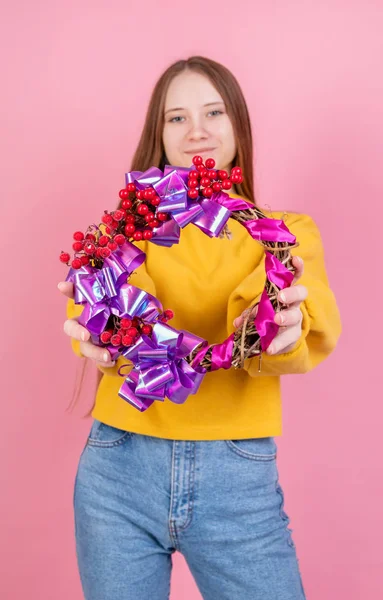 Ung kvinna som håller en ljus Alla hjärtans dag krans på rosa rygg — Stockfoto