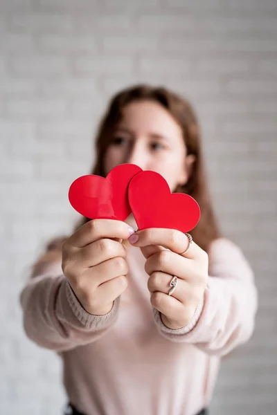 Молодая женщина держит две красные формы сердца на белом кирпичном фоне стены — стоковое фото