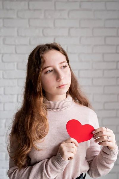 Молодая белая женщина, держащая сердце на белом кирпичном фоне — стоковое фото