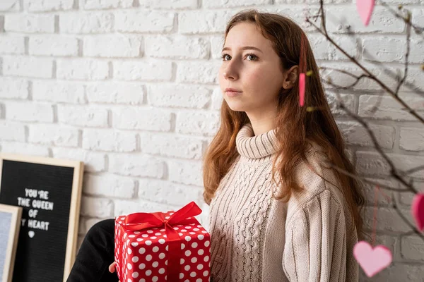 Mujer joven sosteniendo caja de regalo roja sobre fondo de pared de ladrillo blanco — Foto de Stock