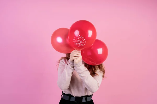 Kobieta zakrywająca twarz trzema czerwonymi balonami słowami I Love You wyizolowanymi na różowym tle — Zdjęcie stockowe