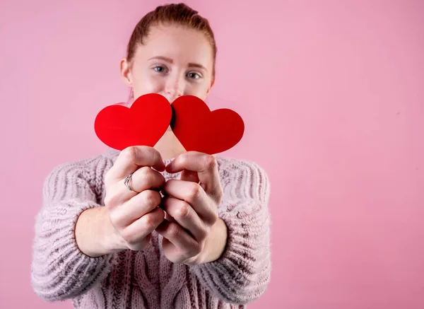 Молодая женщина держит две красные формы сердца на розовом фоне с копировальным пространством — стоковое фото