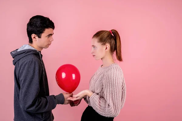 Несчастливая пара глядя друг на друга держа красный шарик изолированный на розовом фоне — стоковое фото