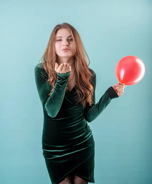 Beautiful young woman in a green dress blowing a kiss to somebody isolated on blue background — 스톡 사진