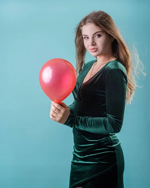 Sexy woman in green dress holding a red balloon on blue background — 스톡 사진