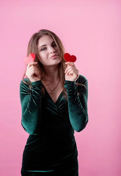 Sexy kobieta w zielonej sukience trzymając kształty serca przed oczami izolowane na różowym tle — Zdjęcie stockowe