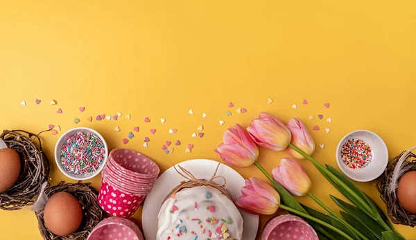Paskalya pastası laleler, yumurtalar ve fırınlama öğeleri ile sarı arka planda fotokopi alanı ile üst görünüm