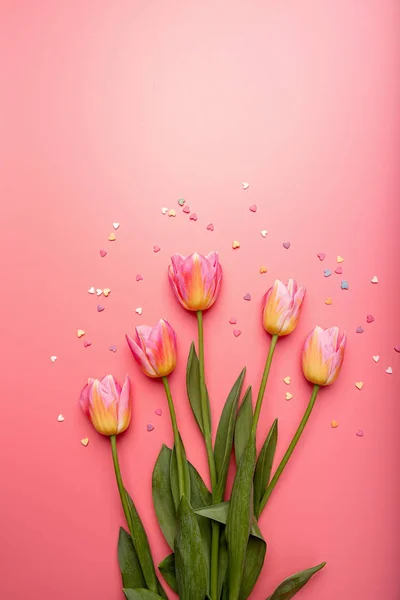 Tulipani rosa e gialli decorati con piccole forme a cuore su sfondo rosa piatto lay vista dall'alto con spazio copia — Foto Stock