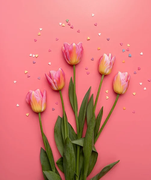 Tulipani rosa e gialli decorati con piccole forme a cuore su sfondo rosa piatto lay vista dall'alto con spazio copia — Foto Stock