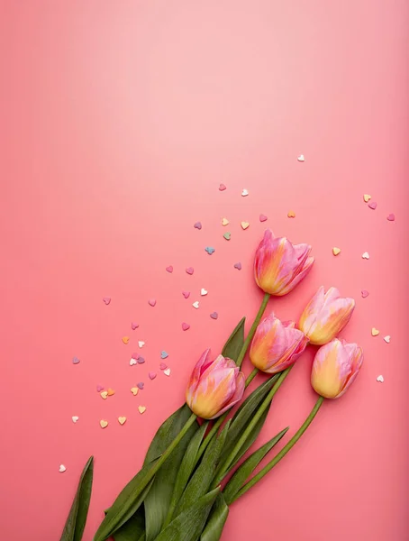Tulipani rosa e gialli decorati con piccole forme a cuore su sfondo rosa piatto lay vista dall'alto con spazio copia — Foto Stock