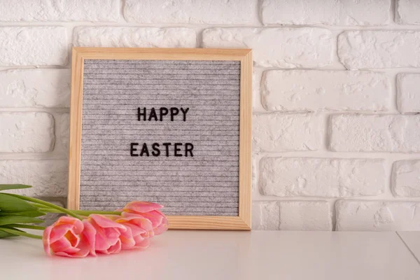 vase with tulips and gray felt letter board with words Happy Easter on white bricks background