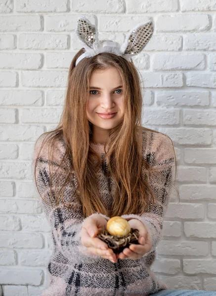 Mujer linda en orejas de conejo sosteniendo un pequeño nido con un huevo en la mano —  Fotos de Stock