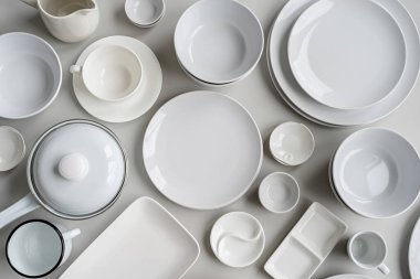 piles of white ceramic dishes and tableware top view on gray background