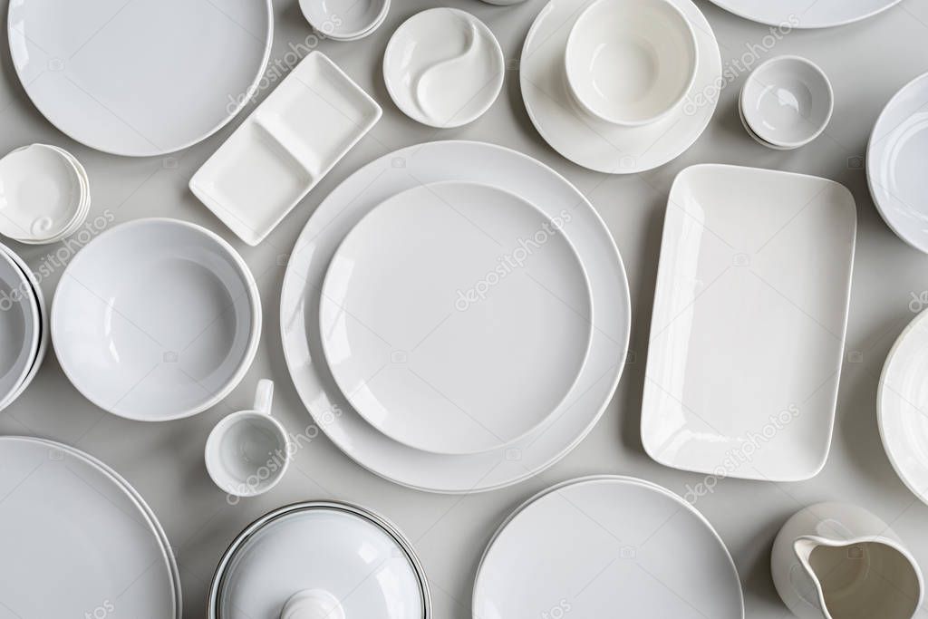 piles of white ceramic dishes and tableware top view on gray background