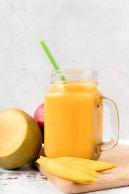 mango smoothie in a mason jar decorated with slices of mango front view on wooden background