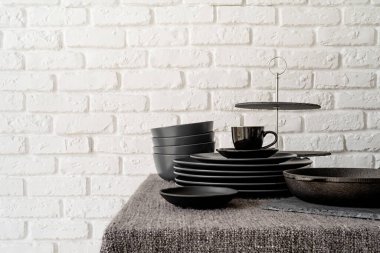 stack of black ceramic dishes and tableware on the table on white brick wall background