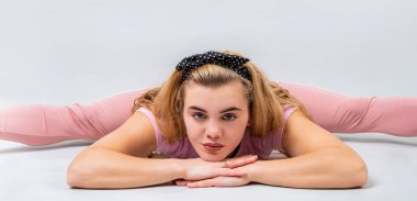 Fitness, spor, eğitim ve yaşam tarzı konsepti. Stüdyoda, gri arka planda izole edilmiş, bacak arası poz veren pembe spor giysili genç bir kadın.