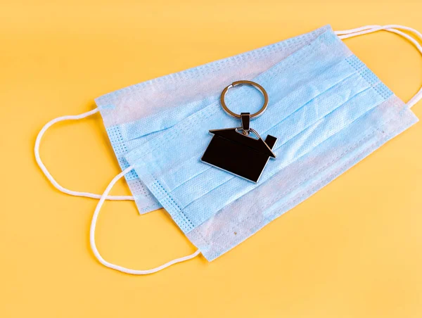 Stay home. Self quarantine. Medical masks and a house shaped keyring on yellow background